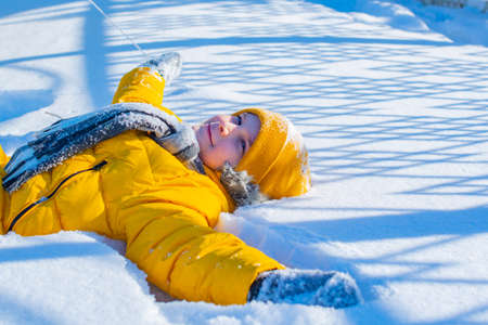 a boy in a yellow jacket lies in a snowdriftの写真素材