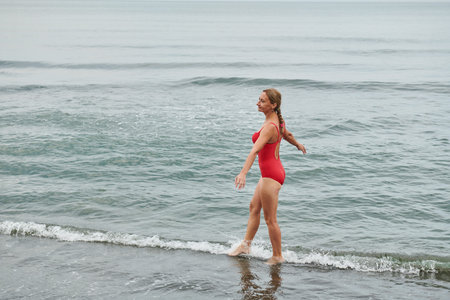 girl in a red swimsuit walking on the beachの写真素材