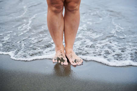 a girl stands on black sand in a waveの写真素材