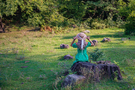 a girl in a green dress is sitting on a stumpの写真素材
