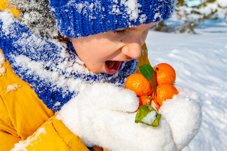 a boy eats tangerines in winter on the street in white mittensの写真素材