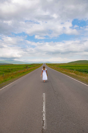 A girl in a white dress is walking along the road