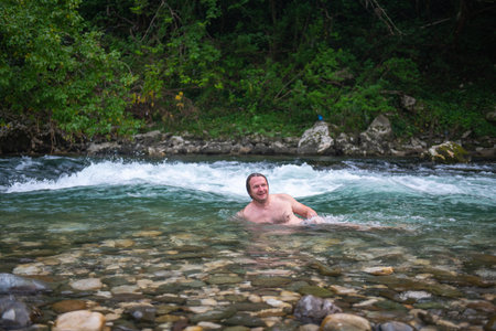 Adventurous man with long hair swimming in a scenic mountain river surrounded by rocks and treesの写真素材