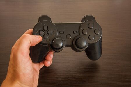 The gamer holds a black dusty video game console joystick in his hand. Play game with a controller. The concept of No time for games, console collecting dustの写真素材