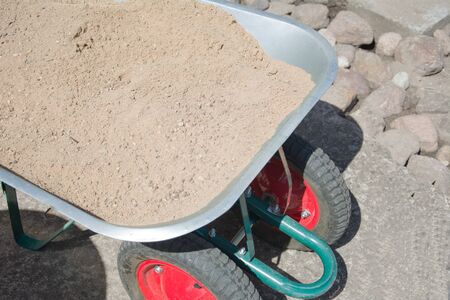 New metal wheelbarrow with sand on construction sites. For cement mixing process to fill the Foundationの写真素材