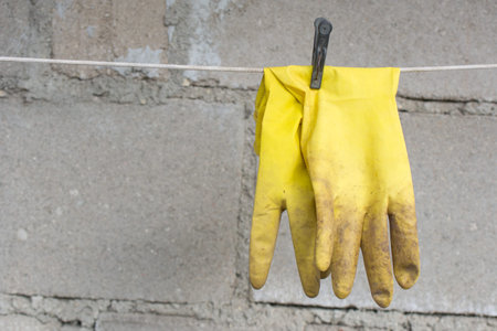 Dirty yellow used medical rubber gloves on the rope with clothespin on concrete background