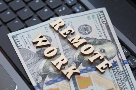 The inscription remote work against the background of a working laptop and money. The office is Quarantined, work from home. The concept of Freelancer working in Internetの写真素材