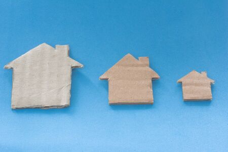 Different Size Of Houses Arranged In Row on blue background. Three differently sized cardboard models of houses. Rent, purchase, delivery of housing and real estate conceptの写真素材