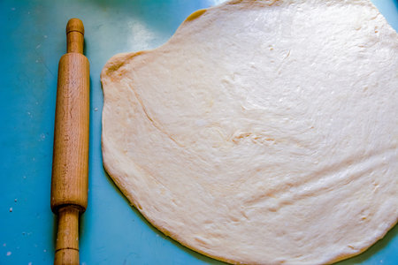 Baking Ingredients. Fresh raw dough with rolling pin on wooden background. Bakery concept