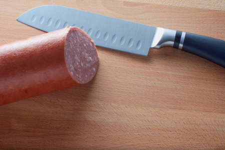 Salami and chef knife on cutting board, top view. Piece of sausage with cutter on kitchen tableの写真素材