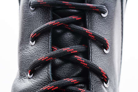 Stylish new shoe isolated on white background. Black leather safety shoe. Red black shoelaces closeup view. Rough leather textureの写真素材