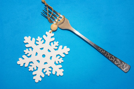 Merrry Christmas and Happy New Year creative table setting. Snowflake and fork on blue painted...