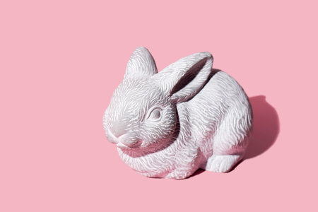 White Easter bunny rabbit with trendy shadow sitting on pink background. Easter symbol