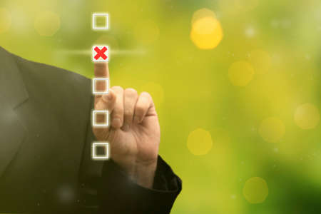 Businessman hand touching and pointing right choice marked with red cross, best option on blurred green background. Strategy of choice. Business planning goal target conceptの写真素材