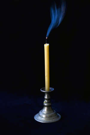 The extinct candle in a candlestick smokes on a black background.の写真素材
