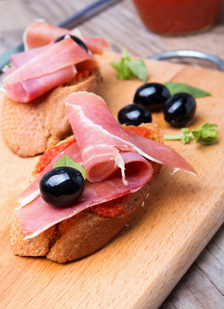 Delicious bruschetta with tomato sauce and prosciutto on the wooden boardの写真素材