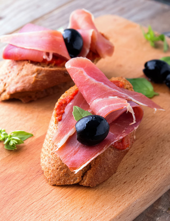 Delicious bruschetta with tomato sauce and prosciutto on the wooden boardの写真素材