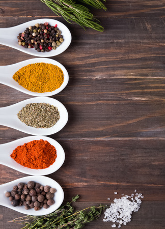 Dry spices in spoons and green herbs on the wooden table, top viewの写真素材