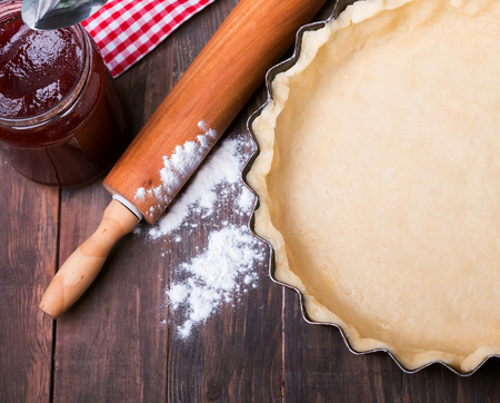 Making a tart. Baking pan with raw dough, rolling pin and flour on the wooden tableの写真素材