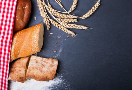 Different kinds of bread, wheat and flour on the black background, top view