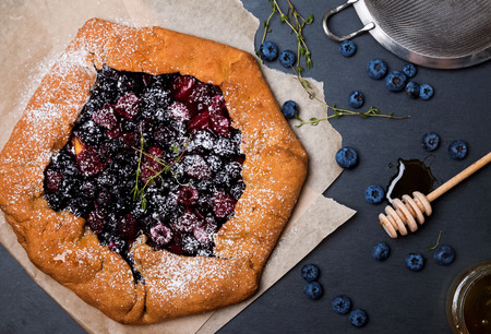 Dark style photo of rustic crispy pie with blueberries and thyme on the black background, top viewの写真素材