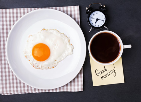 Fried egg, coffee and alarm clock on the black background, top viewの写真素材