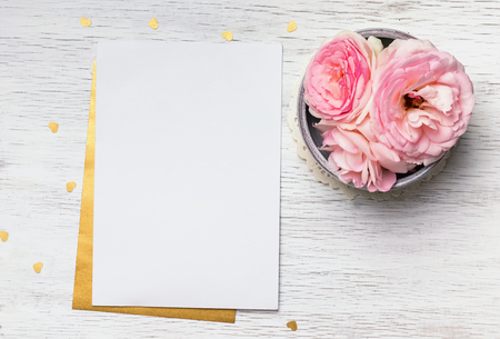 Blank paper and cute pink flowers on white wooden table, top viewの写真素材