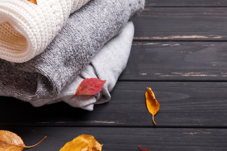 Cozy sweaters and autumn leaves on the black wooden table close-upの写真素材