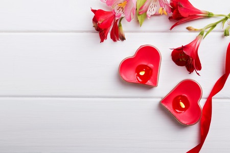 Two heart shaped candles and flowers on the white wooden table. Valentine's day template.の写真素材