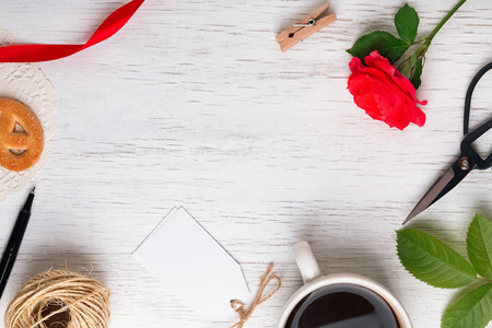 Red rose, coffee, scissors and other small objects on the white wooden table, top viewの写真素材