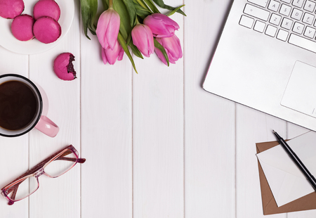 Womans workplace with laptop, coffee pink tulips and macarons.の写真素材