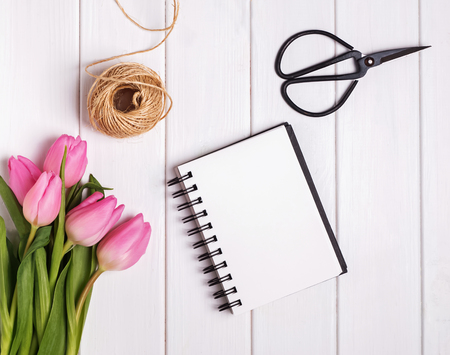 Pink tulips and empty notepad on the wooden table, top viewの写真素材