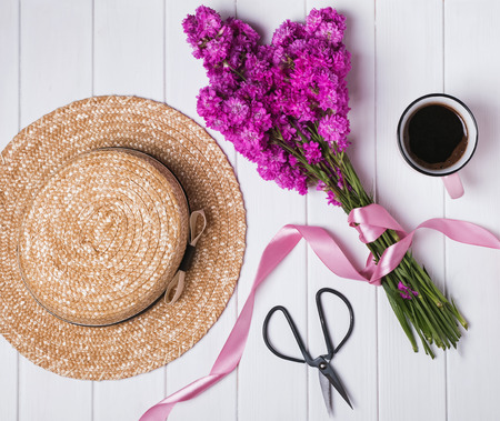 Summer accessories. Straw hat and pink flowers on the white wooden table, top viewの写真素材