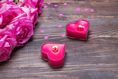Pink roses and two heart shaped candles on the wooden background close-upの写真素材