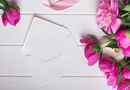 Beautiful peonies and blank paper in white envelope, top viewの写真素材