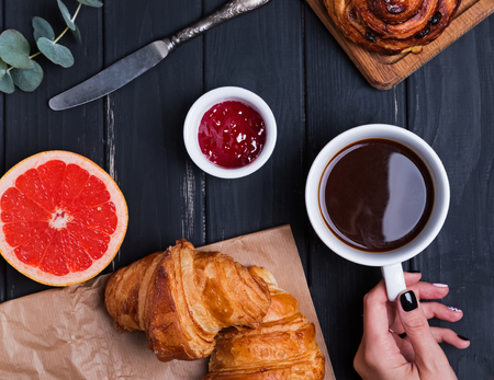 Delicious breakfast with croissants and woman's hand holding cupof coffee on the black table, view from aboveの写真素材