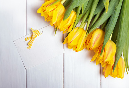 Beautiful yellow tulips and blank pape card on the white tableの写真素材