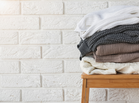Stack of winter sweaters on the white brick wall background.の写真素材