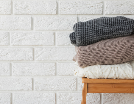 Stack of cozy winter sweaters on the white brick wall background.の写真素材