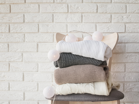 Stack of knitted sweaters and garland with lights on the brick wall backgroundの写真素材