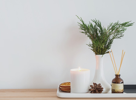 Cozy modern home details. Burning candle, aroma sticks and other elements in the small table near the white wall.の写真素材