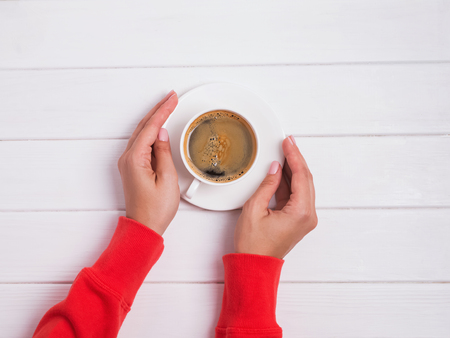 Woman's hands in bright red clothing holding a cup of fresh coffee, top view.の写真素材