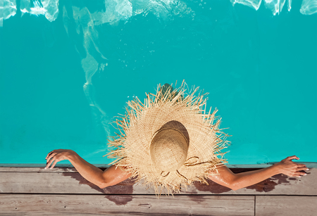 Woman in big straw hat sitting in the swimming poolの写真素材