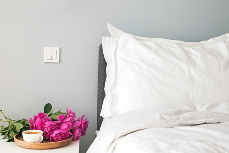 Bed with white bed sheets and pink peonies and coffee on the nightstand.の写真素材