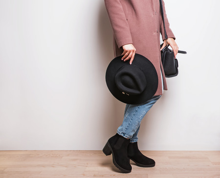 Autumn fashion. Woman in beige coat and stylish boots holding a hat in hand.の写真素材