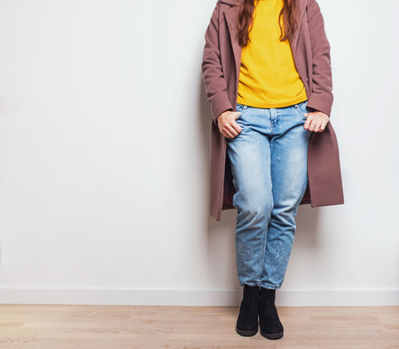 Autumn feminine fashion outfit in details. Woman wearing jeans and coat near the white wall.の写真素材