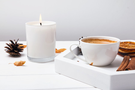 Autumn coffee break. Cup, cinnamin, dry oranges and leaves and burning candle close-upの写真素材