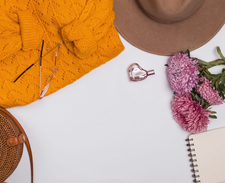 Feminine autumn accessories: felt hat, yellow sweater, bag and flowers.