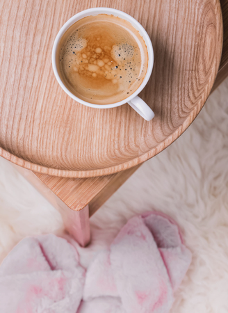 Coffee on the wooden tray standing on the small table and pink slippers on the floor.の写真素材