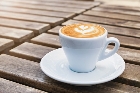 Cup of fresh cappuchino with heart drawn on the foam on the street wooden table close-upの写真素材